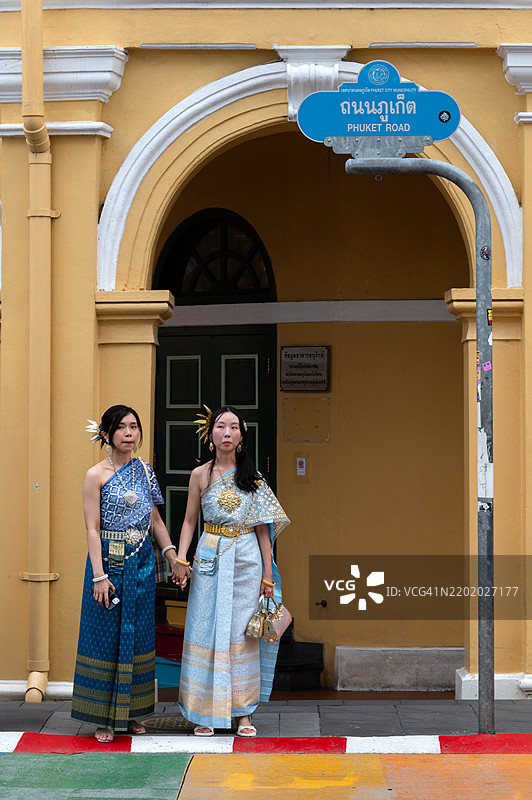 游客们穿着传统泰国服装，站在普吉镇普吉路的特许银行大楼前。图片素材