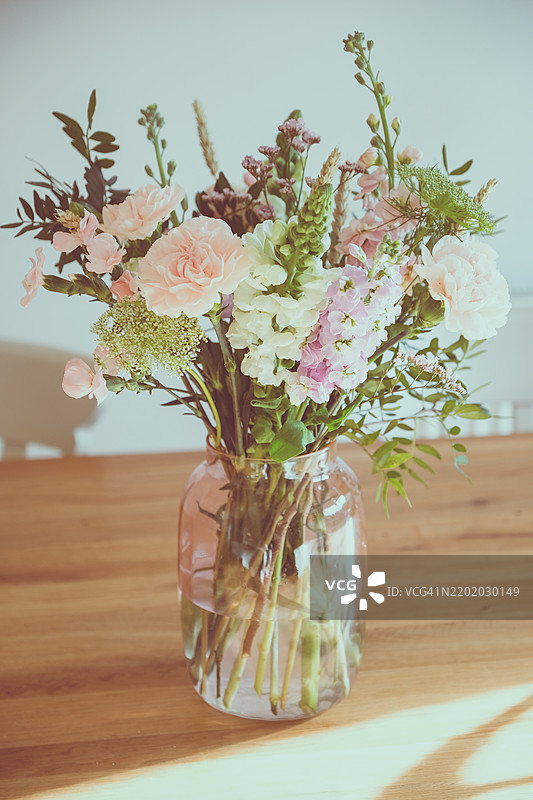 美丽的花束放在透明花瓶中，包含康乃馨、金鱼草、马提奥拉、开心果叶和海洋花。图片素材