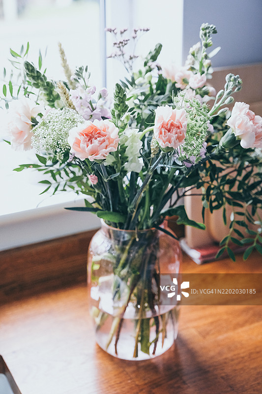 美丽的花束放在透明花瓶中，包含康乃馨、金鱼草、马提奥拉、开心果叶和海洋花。图片素材