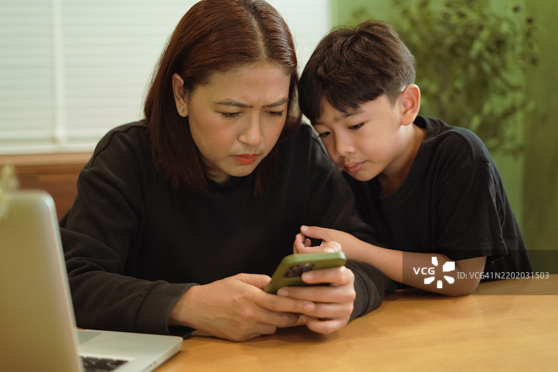 男孩正在和他的母亲一起看手机。图片素材