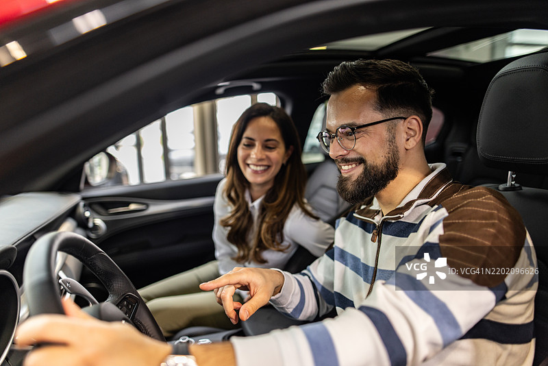 快乐的情侣在汽车展厅试驾全新汽车图片素材