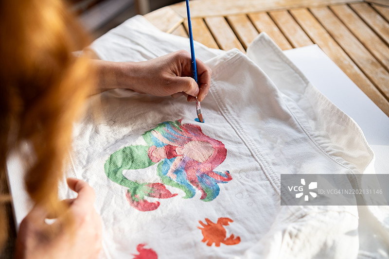 女人在白色牛仔夹克上绘制美人鱼和螃蟹的图案图片素材