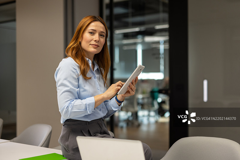 自信的女商人在办公室轻松坐着，使用数字平板电脑，展现现代商业责任的方式图片素材