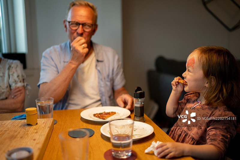 祖父和孙女在家吃披萨。图片素材