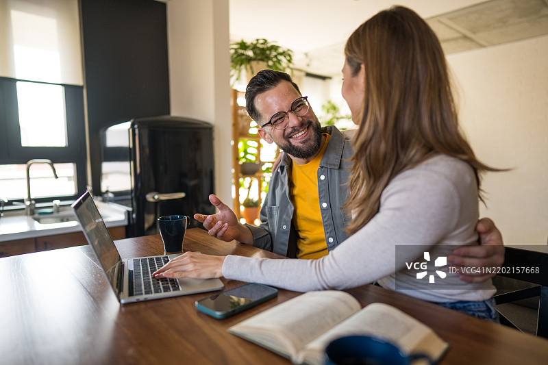 快乐的情侣在家用笔记本电脑工作并微笑图片素材