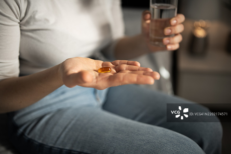 女人准备服用药物，手里拿着药丸和一杯水。图片素材