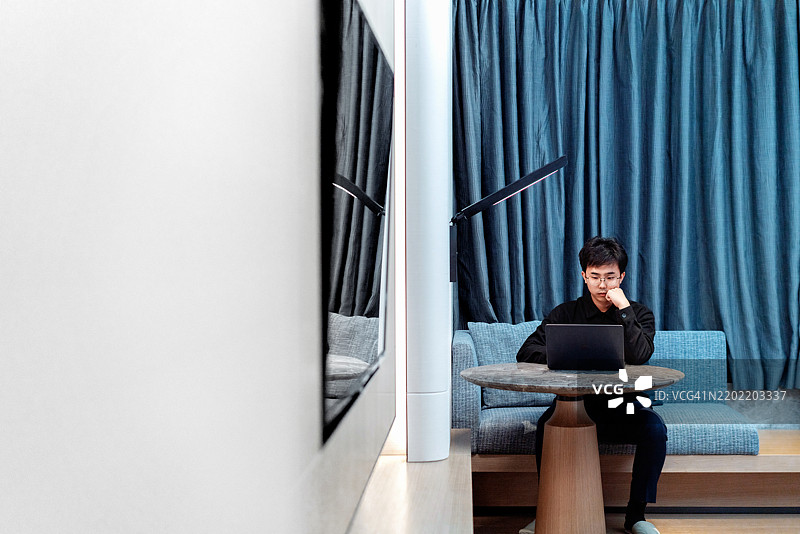 商人在酒店房间内出差时使用笔记本电脑工作。图片素材