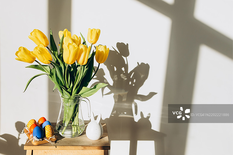 复活节装饰。阳光下的静物：黄色郁金香、复活节兔子和彩色鸡蛋。图片素材