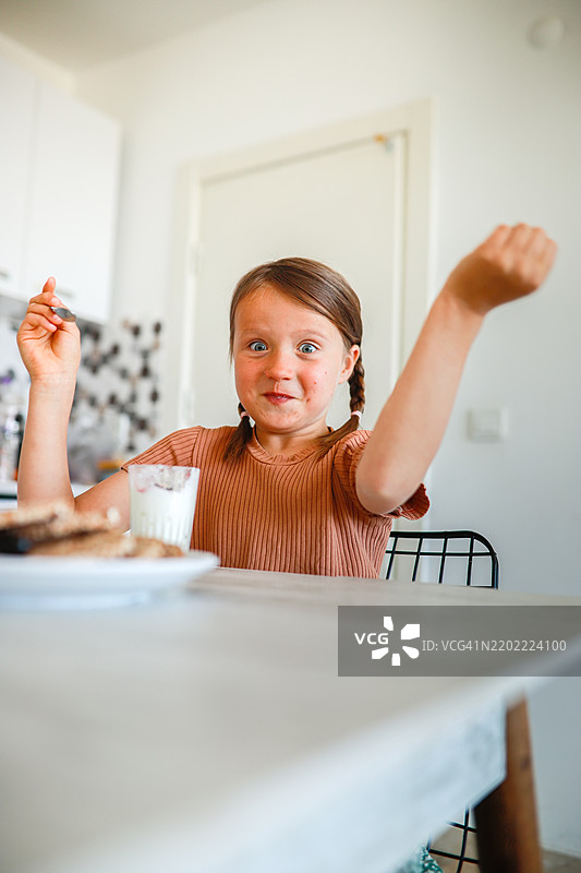 一个扎着两个辫子的快乐女孩在准备上学时享受酸奶，甜美的早晨时光。图片素材