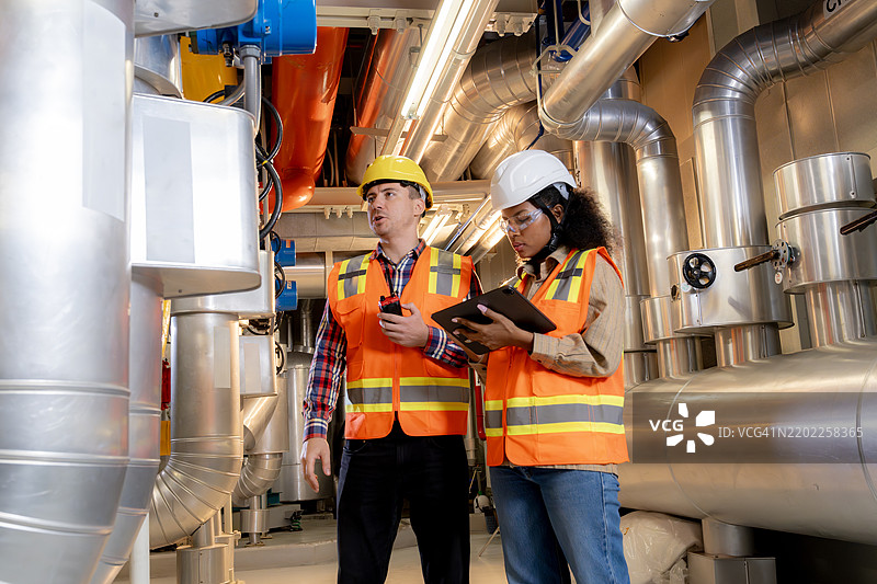 两名工程师在建筑的冷却控制室检查管道系统。图片素材