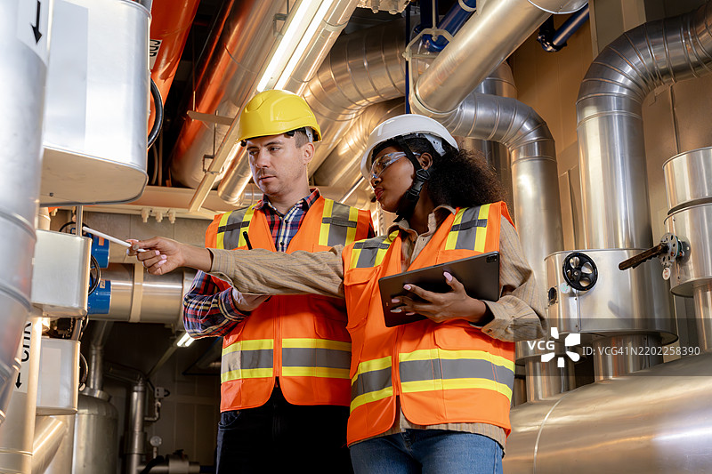 两名工程师在建筑的冷却控制室检查管道系统。图片素材