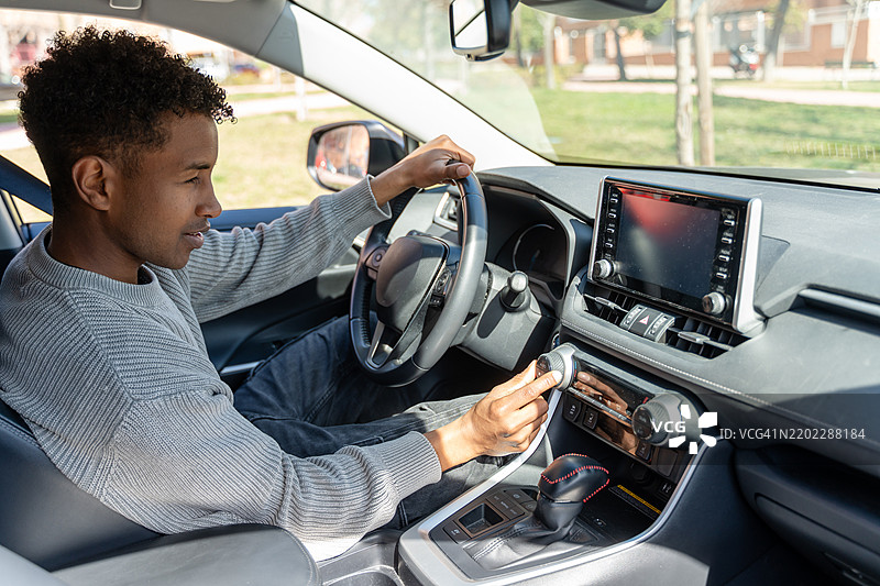 年轻男子驾驶现代汽车并调节音响系统的音量图片素材
