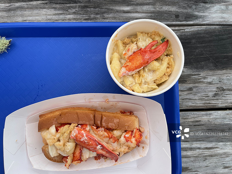 新鲜的龙虾卷野餐，来自码头。野餐桌上的龙虾通心粉与奶酪，俯瞰着水面。图片素材