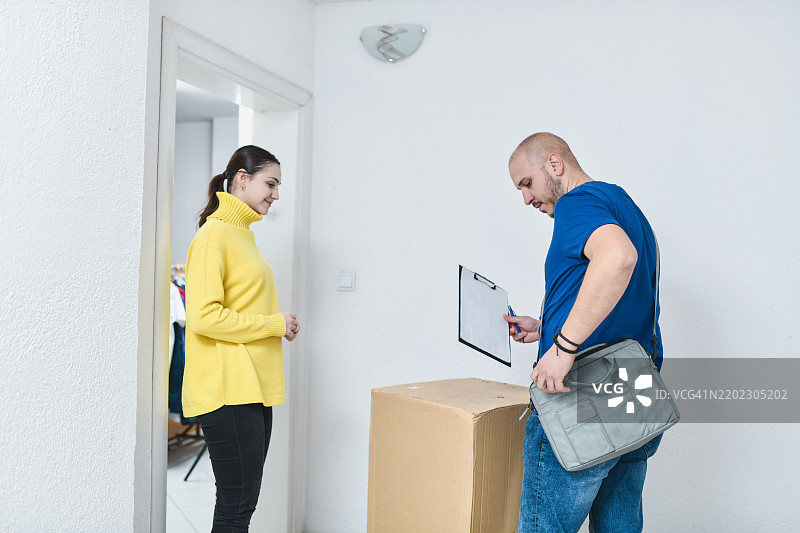 愉快的女性在签署文件前等待领取大包裹图片素材