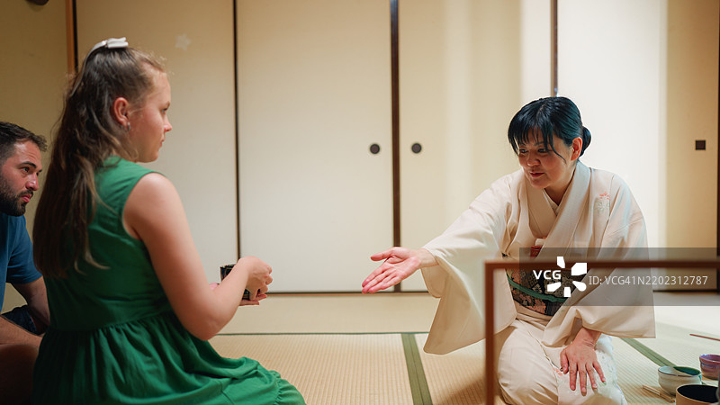 日本女性茶道大师在传统的日本茶室为年轻游客夫妇准备抹茶茶。图片素材