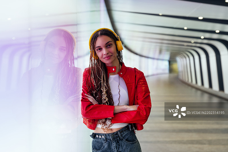 微笑的女性双臂交叉，戴着耳机在地下隧道中听音乐图片素材