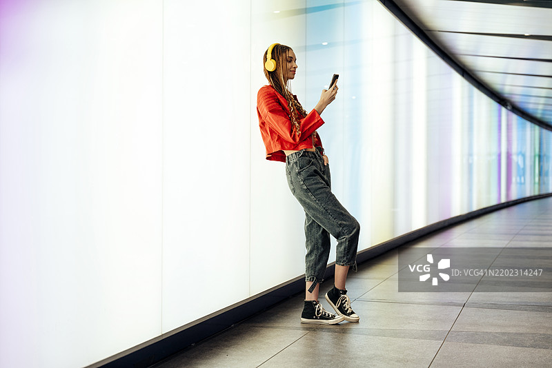 年轻女性在灯光照明的地下隧道中听音乐并使用智能手机图片素材