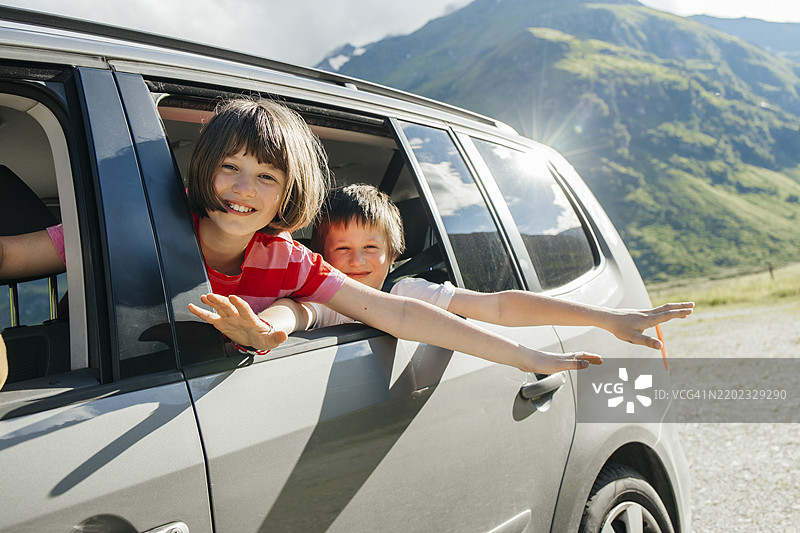 快乐的兄妹在山附近的车里旅行图片素材