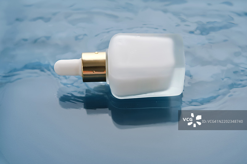 蓝色背景下水中漂浮的白色保湿精华瓶图片素材