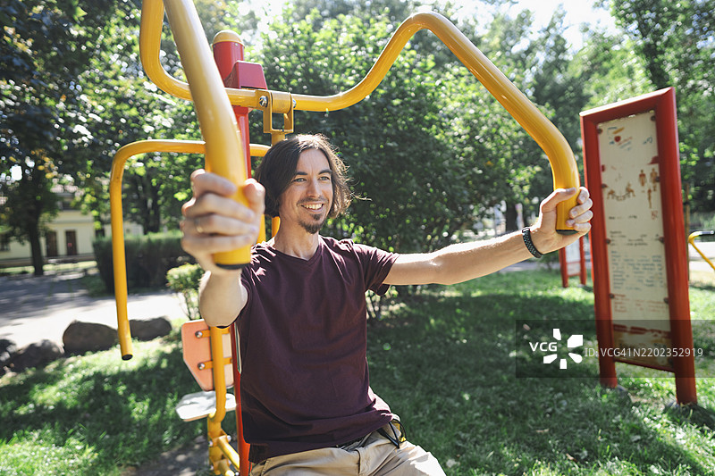 在公园里使用户外健身器材的微笑男子图片素材