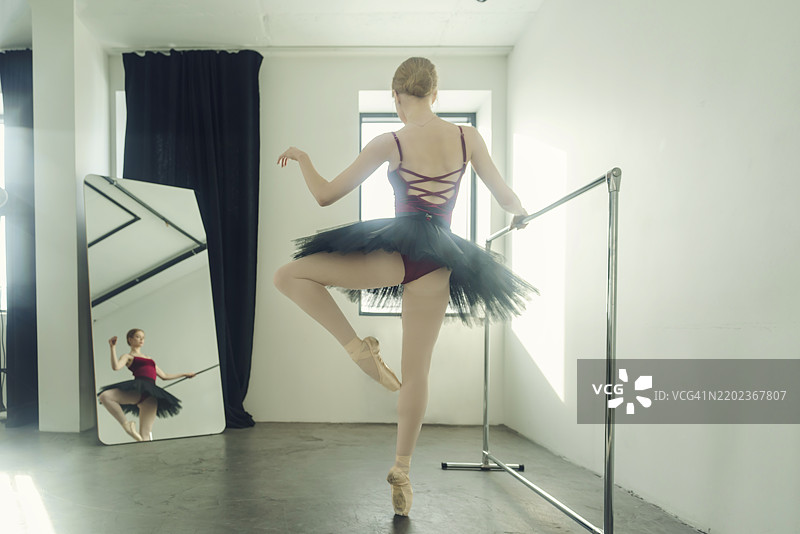 年轻的芭蕾舞者穿着芭蕾舞裙和尖头鞋，站在芭蕾舞杠旁，在逆光中展示芭蕾舞姿势，位于俄罗斯西伯利亚的诺沃西比尔斯克。图片素材