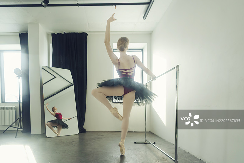 年轻的芭蕾舞者穿着芭蕾裙和尖头鞋，站在芭蕾杆旁，在逆光中展示芭蕾元素，位于俄罗斯西伯利亚的诺沃西比尔斯克。图片素材
