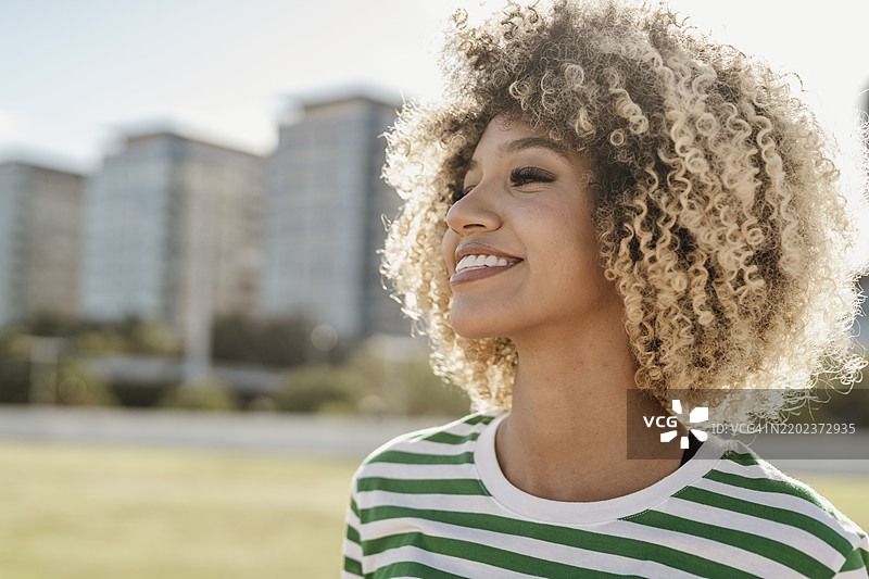 阳光明媚的日子里，微笑的美丽卷发女性图片素材