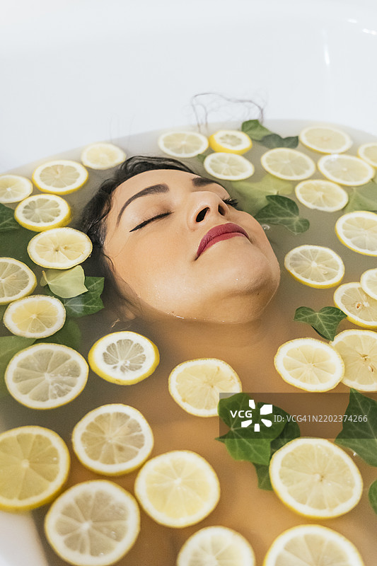 年轻女性在浴缸中放松，周围有柠檬片和叶子图片素材