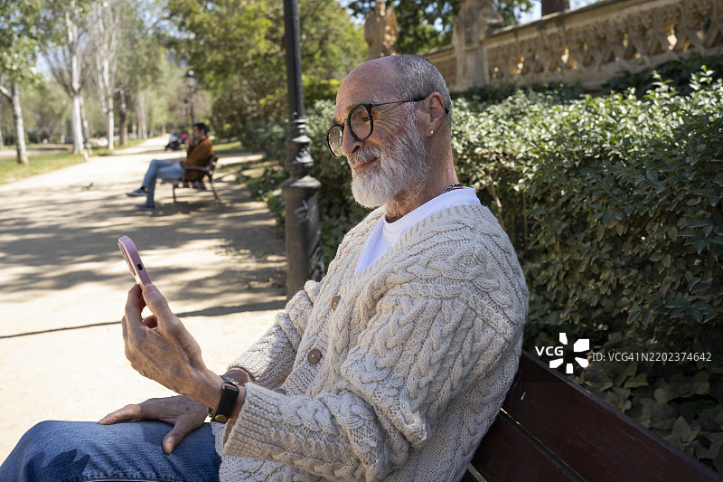 微笑的老年男子在公园里通过手机进行视频通话图片素材