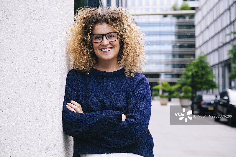 快乐的女人双臂交叉倚靠在建筑物前的墙上图片素材