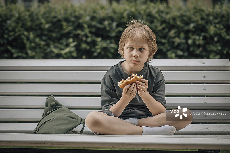 男孩在公园长椅上吃汉堡图片素材