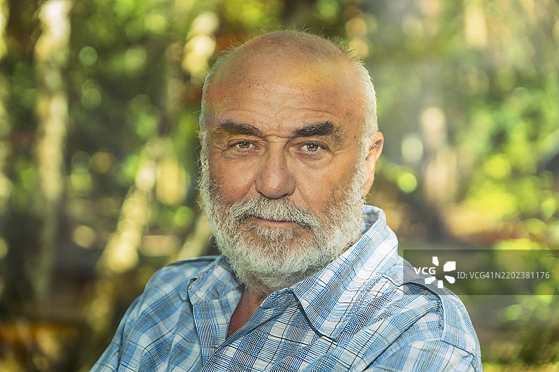 一位有着灰色胡须的老年男子站在森林前面图片素材