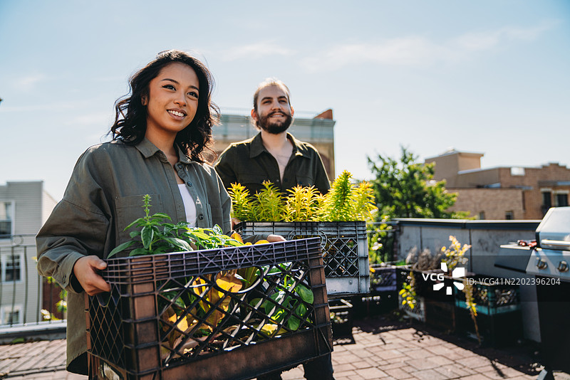 一对时尚的千禧一代情侣正在屋顶上散步，照顾他们的蔬菜花园。图片素材