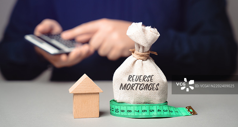 反向抵押贷款概念：一种面向62岁或以上房主的贷款类型，允许他们将房屋的部分净值转换为现金。商业与金融，钱袋与商人。图片素材