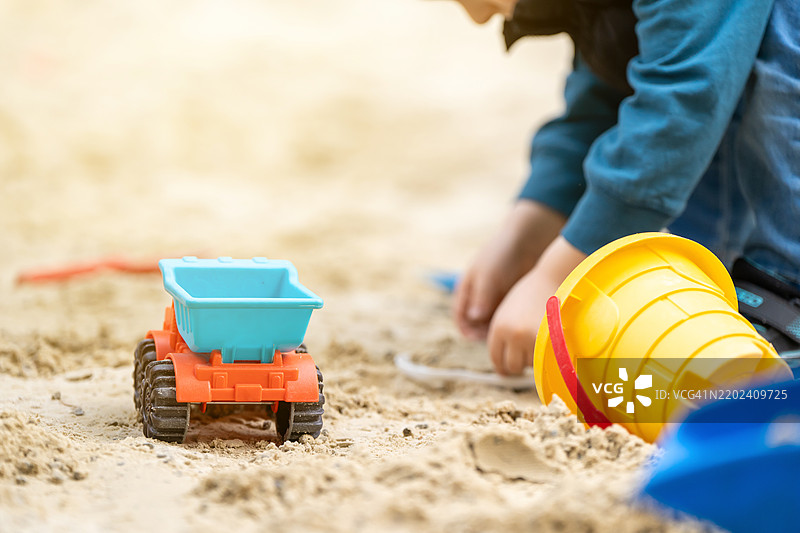 可爱的小男孩在阳光明媚的春天里玩沙箱，进行户外创意活动，玩具卡车和水桶，重点在于汽车。图片素材