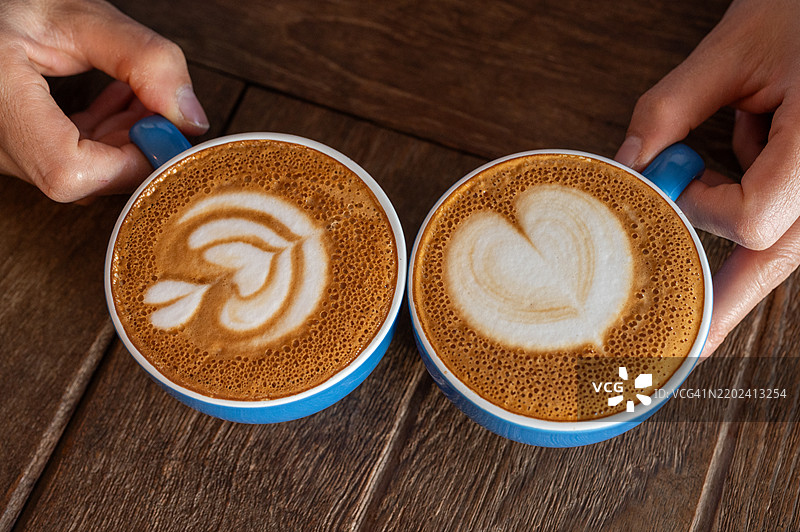 手握两杯热卡布奇诺咖啡的特写镜头，准备饮用。图片素材