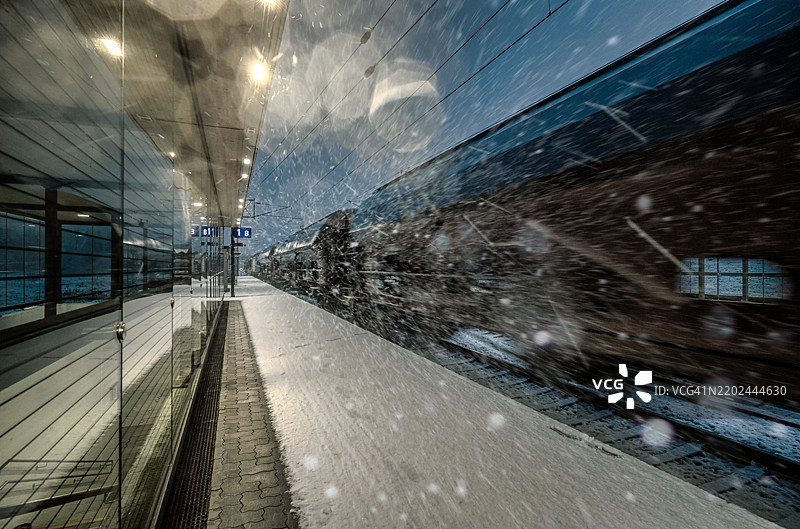 夜晚的火车站，雪花纷飞，一列快速列车驶过。图片素材