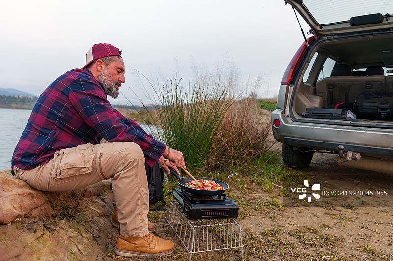 成熟男子在湖边烹饪，旁边停着他的四轮驱动汽车图片素材