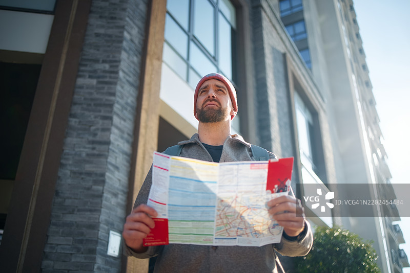 年轻男子在阳光明媚的日子里手持地图探索城市街道图片素材