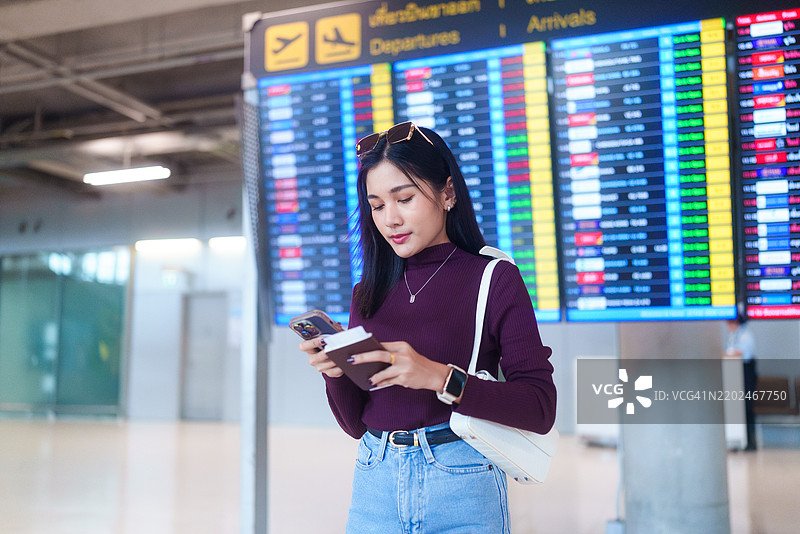 美丽的亚洲女性在机场数字出发牌前查看航班信息。图片素材
