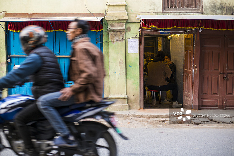 一个人骑着摩托车经过尼泊尔加德满都帕坦杜巴广场附近的新ar建筑。图片素材