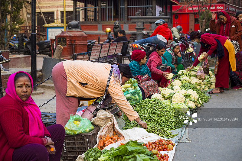 在尼泊尔加德满都的帕坦杜巴广场，一位卖蔬菜的小贩坐在那里。图片素材