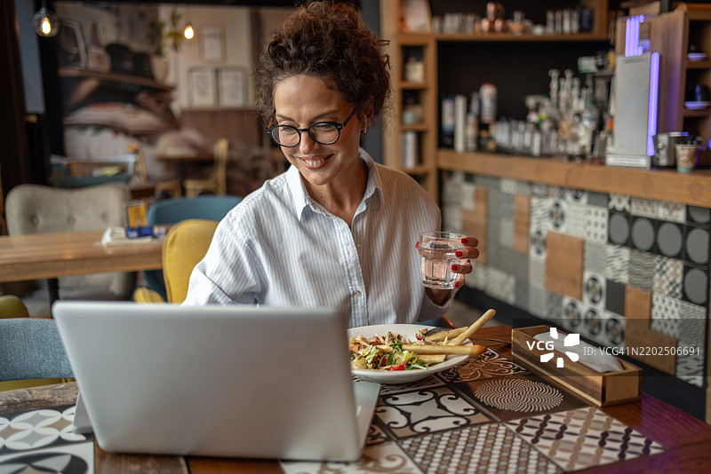在餐厅里，女自由职业者一边用笔记本电脑工作，一边享用午餐图片素材