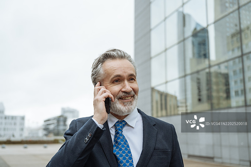 微笑的成熟商人在金融区手持智能手机的肖像图片素材