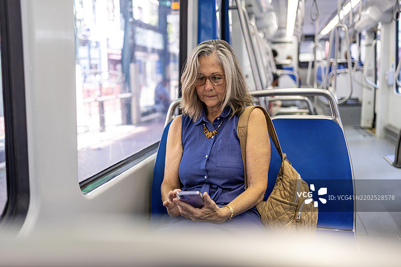 成熟的女性坐在公共交通列车上使用手机图片素材
