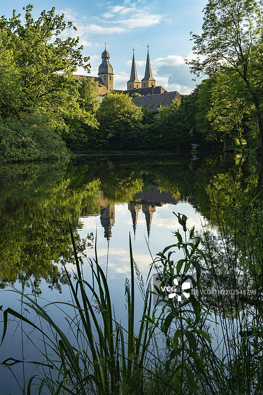 马里恩敏斯特修道院教堂的塔楼倒映在宁静的湖面上,湖边环绕着树木,位于德国北莱茵-威斯特法伦州,欧洲。图片素材