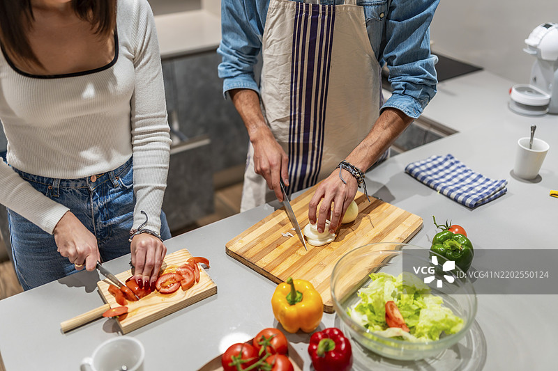 年轻情侣在现代厨房中一起切新鲜蔬菜，准备健康沙拉。图片素材