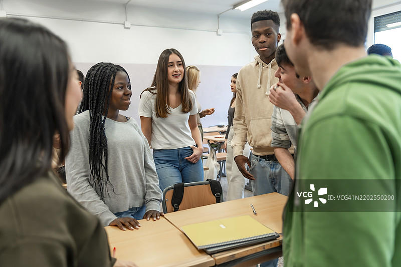 一群多元化的大学生在教室里围坐在桌子旁，进行团队合作，讨论和分享想法。图片素材