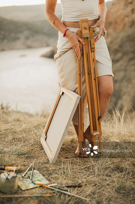 户外女性腿部和手部的特写，旁边有画架。图片素材