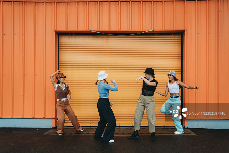 酷炫的舞者们在橙色墙壁前尽情跳舞。图片素材